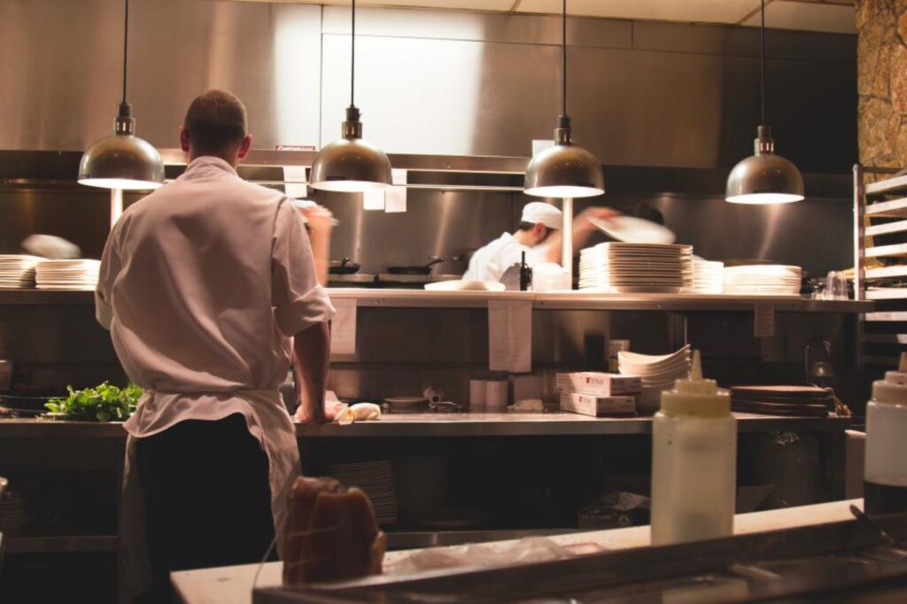 Chef plating meals at the pass of a busy commercial kitchen